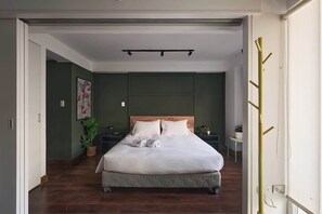 Une chambre à coucher avec un lit, une table de chevet, une lampe, une plante et un porte-manteau.