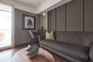 Un salon moderne avec un canapé gris, un tableau encadré au mur, une table basse ronde et un lampadaire.