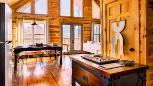 A wooden cabin interior with a dining area, a kitchen counter, and a large window overlooking a deck. - 5* Family Cabin~View~Hot Tub~FirePit~Pools~Bears (Gatlinburg)