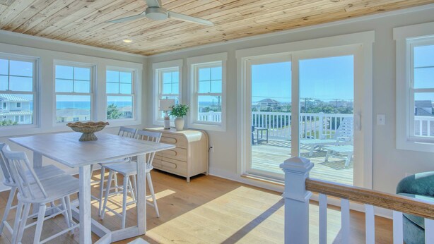 A spacious room with a large dining table, white chairs, a ceiling fan, and large windows offering a view of the ocean. - Atlantis | Ocean Views, Private Saltwater Pool, Elevator, Pets, Beach access (Topsail Beach)