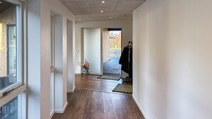 Un pasillo con suelo de madera, una puerta que da al exterior y una ventana a la izquierda.