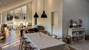 Amplia sala de estar con una mesa de comedor, sillas y un sofá. Cuenta con ventanas grandes que ofrecen luz natural y vistas al exterior.