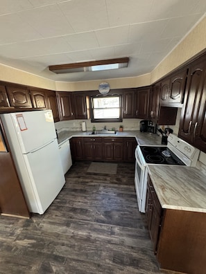 A kitchen with dark wooden cabinets, a white refrigerator, a stove, and a window above the sink. - Spacious 4BR Accessible Lake House w/ Dock Access, Pontoon & Hosting Spaces (Fremont)