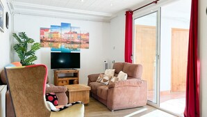 Ein Wohnzimmer mit einer Couch, einem Fernseher, einem Holzschrank und einem großen Fenster mit roten Vorhängen.