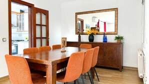 Ein Essbereich mit Holztisch und orangefarbenen Stühlen, einem Holzschrank und einem Spiegel an der Wand.