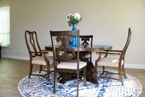 A dining area with a round table, four wooden chairs, a blue vase with flowers, and a blue and white patterned rug. - Charming 3BR Home Peaceful Area Perfect Getaway (Sherman)