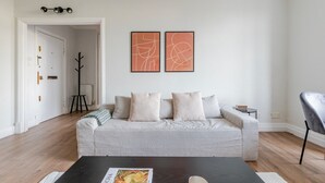 Un salon avec un canapé gris, deux tableaux abstraits, une table basse noire et un fauteuil.