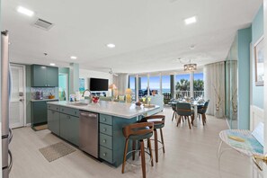 A modern kitchen with a central island, dining area with chairs, and a view of the ocean. - Relax in this spacious 3-bedroom beachfront condo in Panama City Beach! (Panama City Beach)
