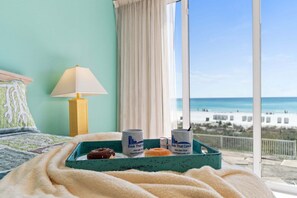 A bed with a view of the beach, a lamp, and a tray with two mugs and a donut. - Relax in this spacious 3-bedroom beachfront condo in Panama City Beach! (Panama City Beach)