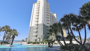 Um hotel alto com várias varandas, piscina e palmeiras.
