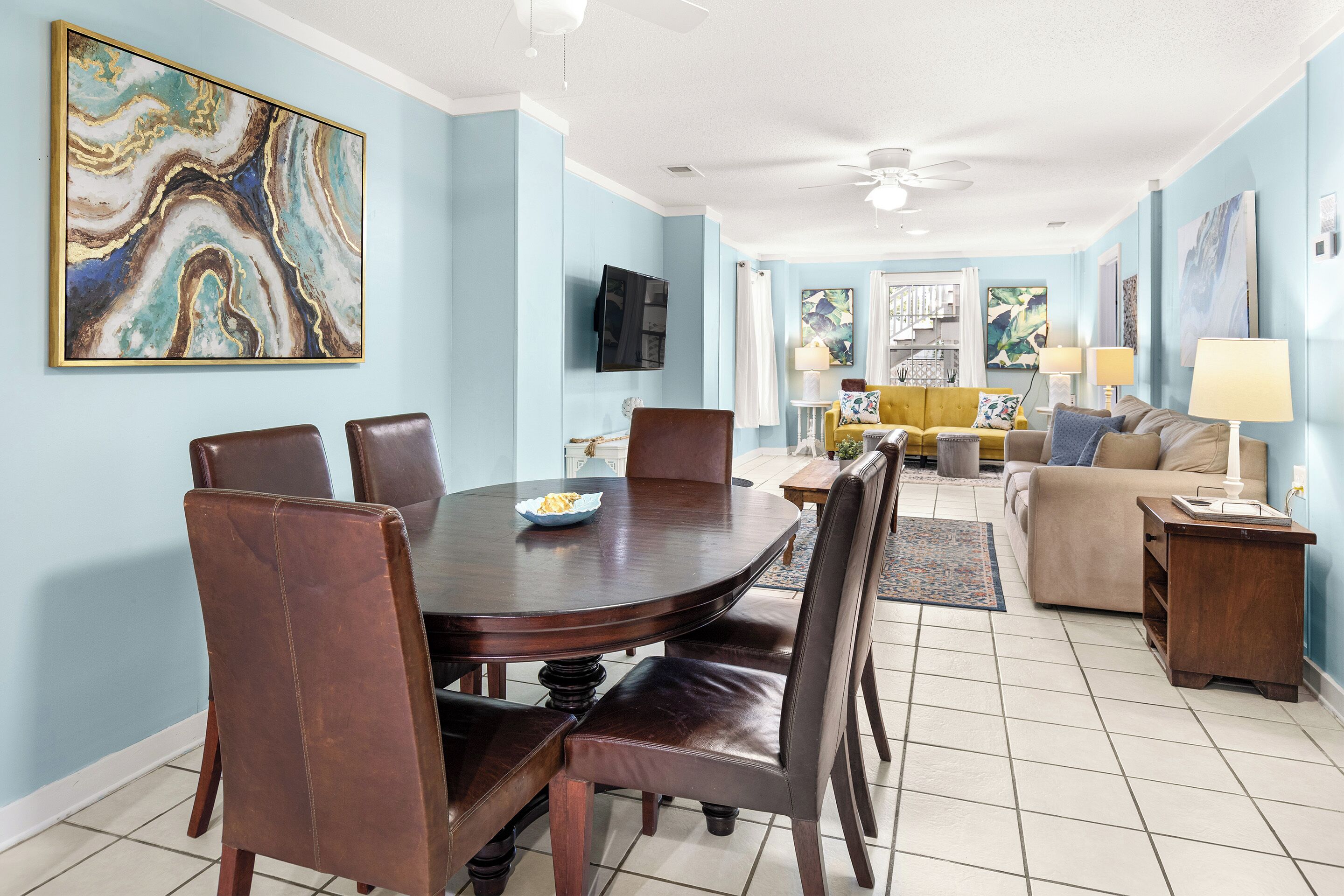 A dining area with a round table and chairs, a living room with a sofa and lamps, and a ceiling fan.