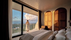 Une chambre avec un grand lit, une vue à travers une porte vitrée et des portes en bois.