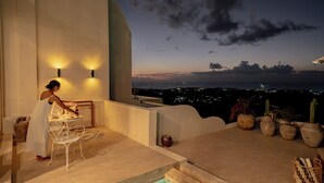 Une terrasse avec une table et des chaises, une vue sur la ville au crépuscule et des plantes en pot.