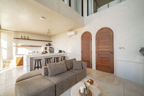 A modern living room with a sofa, a coffee table, and a kitchen in the background. - Villa Mabu (Uluwatu)