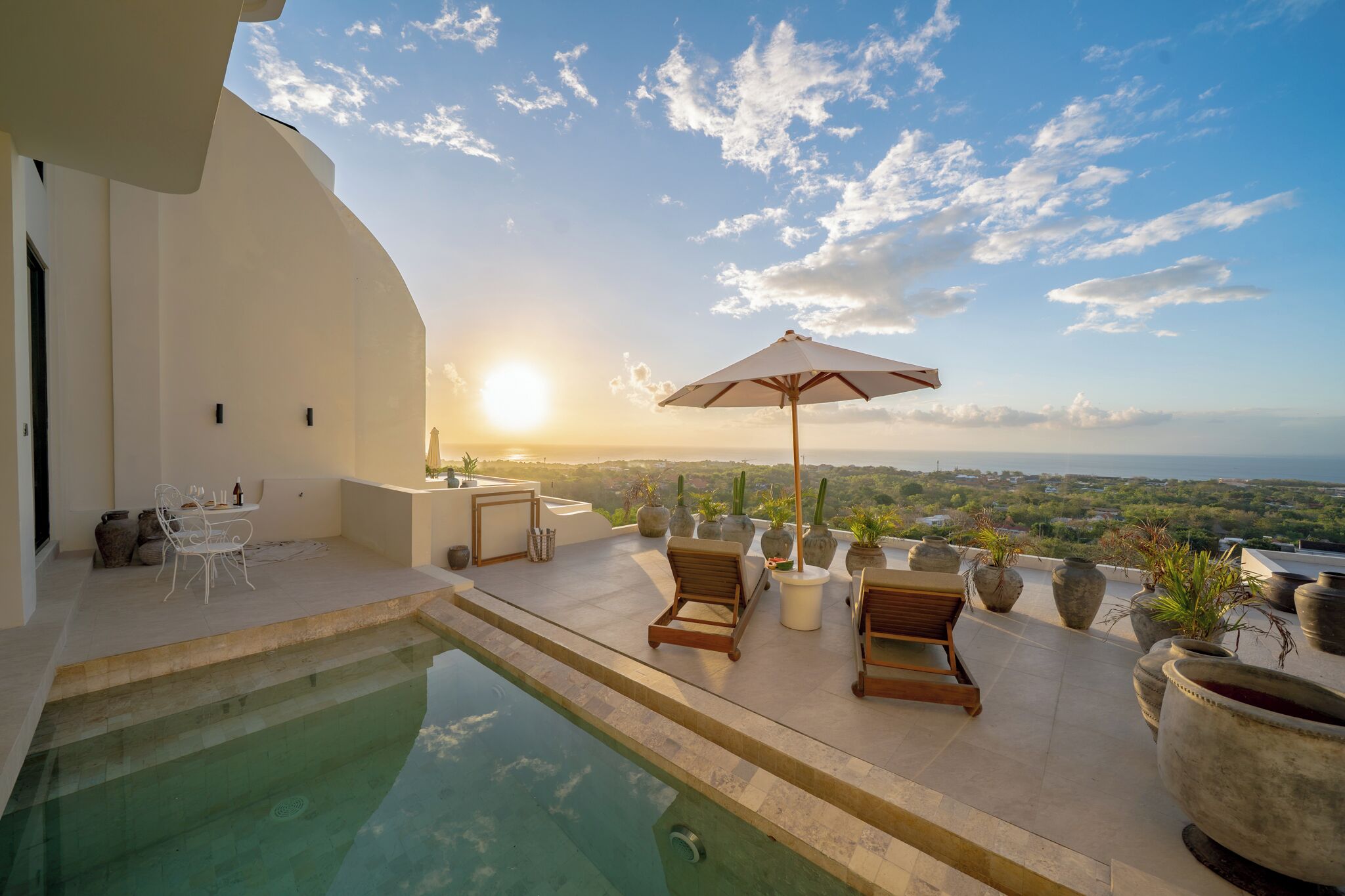Ein Poolbereich mit Liegestühlen und einem Tisch, mit Blick auf eine schöne Landschaft und Sonnenuntergang.