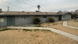 A single-story house with a gray exterior, a front door, and a small front yard with gravel and sparse grass.