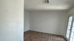 An empty room with hardwood flooring, white walls, a window, and a door.