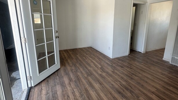 A spacious room with a wooden floor, white walls, and a door with a glass panel.