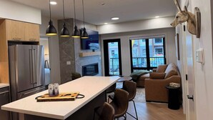 A modern kitchen with a central island, built-in appliances, pendant lighting, and a view to the outside. - Hidden Cirque Hydeaway at Ascent (Canmore)