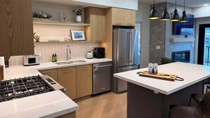 A modern kitchen with a central island, stainless steel appliances, wooden cabinets, and pendant lighting. - Hidden Cirque Hydeaway at Ascent (Canmore)