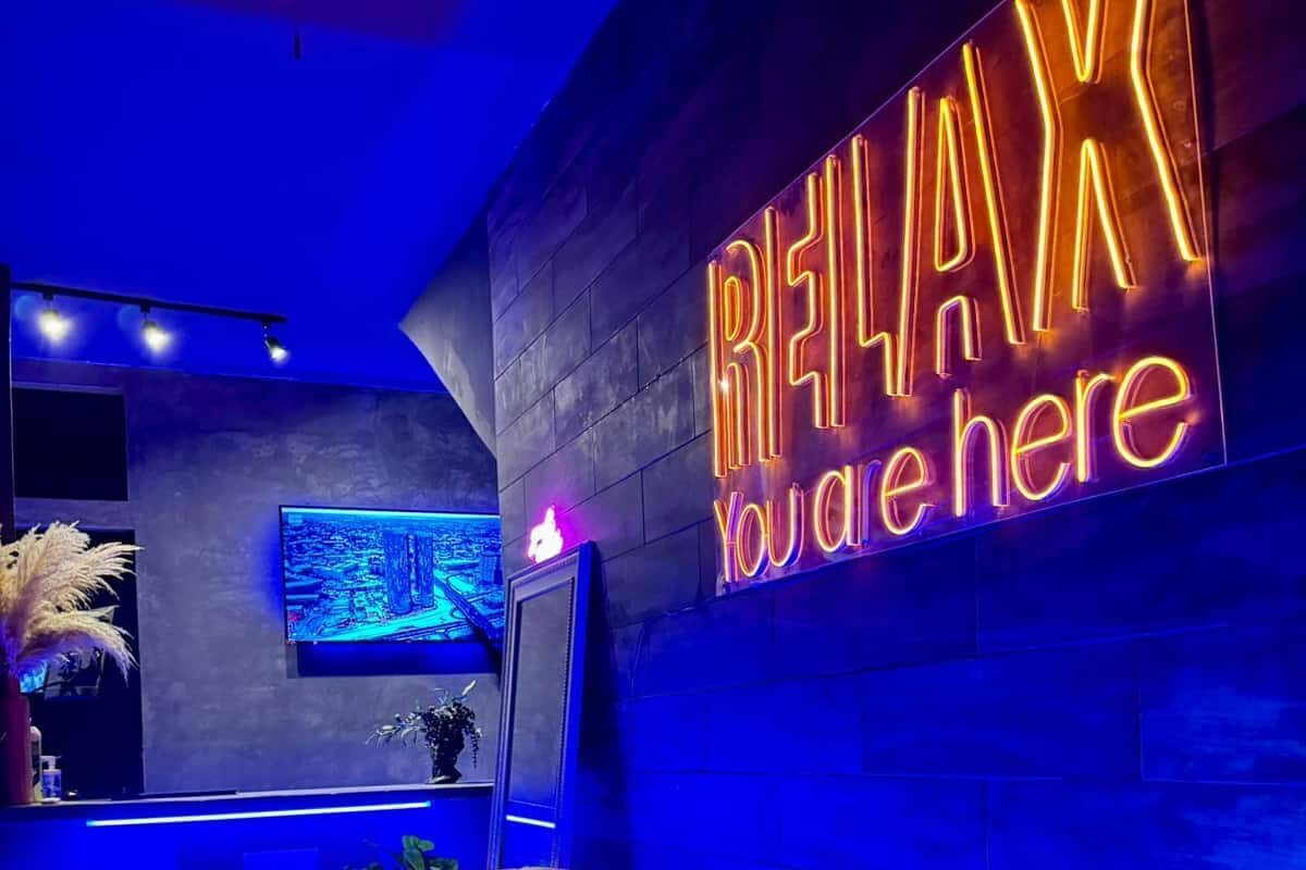 Ein moderner Lounge-Bereich mit einem Neon-Schild mit der Aufschrift "RELAX You are here" und einem bequemen, roten Sofa mit gestreiften Kissen.