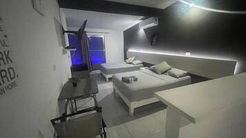 Een moderne, minimalistisch ingerichte slaapkamer met een groot bed, een klein bureau en een stoel. Achtergrond is een kamer met blauwe verlichting.