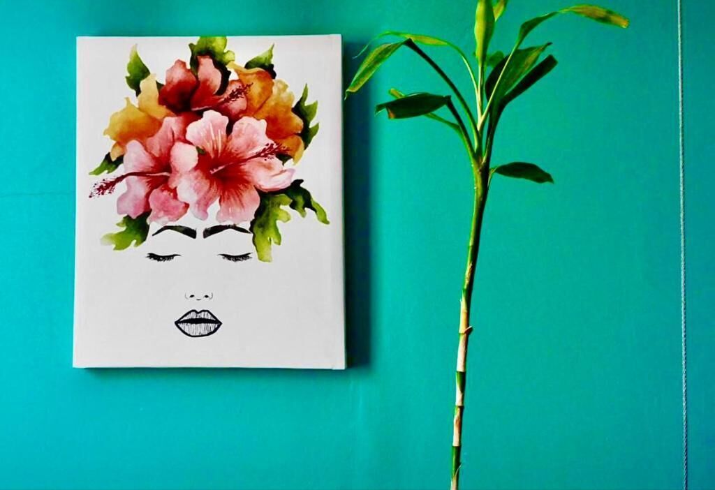A painting of a woman's face with floral elements on a white background, next to a green plant.
