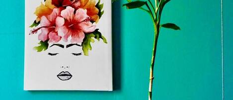 A painting of a woman's face with floral elements on a white background, next to a green plant.