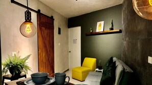 A dining area with a wooden table set for two, a yellow chair, and a sofa. - zyan Rooms (Villahermosa)