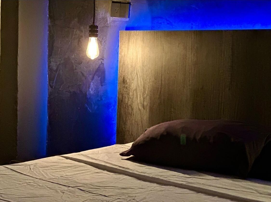 A bedroom with a wooden headboard, a single light bulb, and a pillow on the bed.