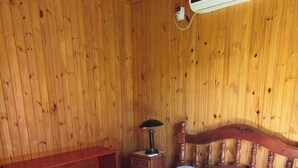 Ein Zimmer mit Holzwänden, einem Bett, einem Nachttisch, einer Lampe und einer Klimaanlage.