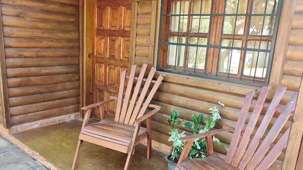 Eine Holzhütte mit zwei Adirondack-Stühlen und einem Fenster mit Gitterstäben.