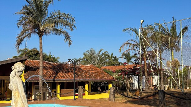A swimming pool with a statue, palm trees, and a building with a tiled roof. - Country house with pool and beautiful gourmet area near Holambra. (Artur Nogueira)