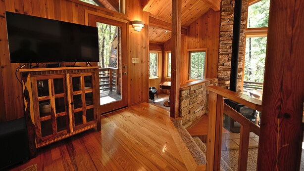 A wooden interior with a flat-screen TV on a cabinet, stone walls, and large windows.