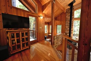 A wooden interior with a flat-screen TV on a cabinet, stone walls, and large windows.