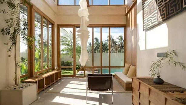 A spacious room with large windows, a hanging light fixture, a wooden bench, and a seating area with cushions. - KOO villa (Pejeng Kawan)