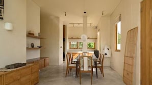 A spacious dining area with a central table and chairs, wooden cabinets, and a view of the kitchen in the background. - KOO villa (Pejeng Kawan)