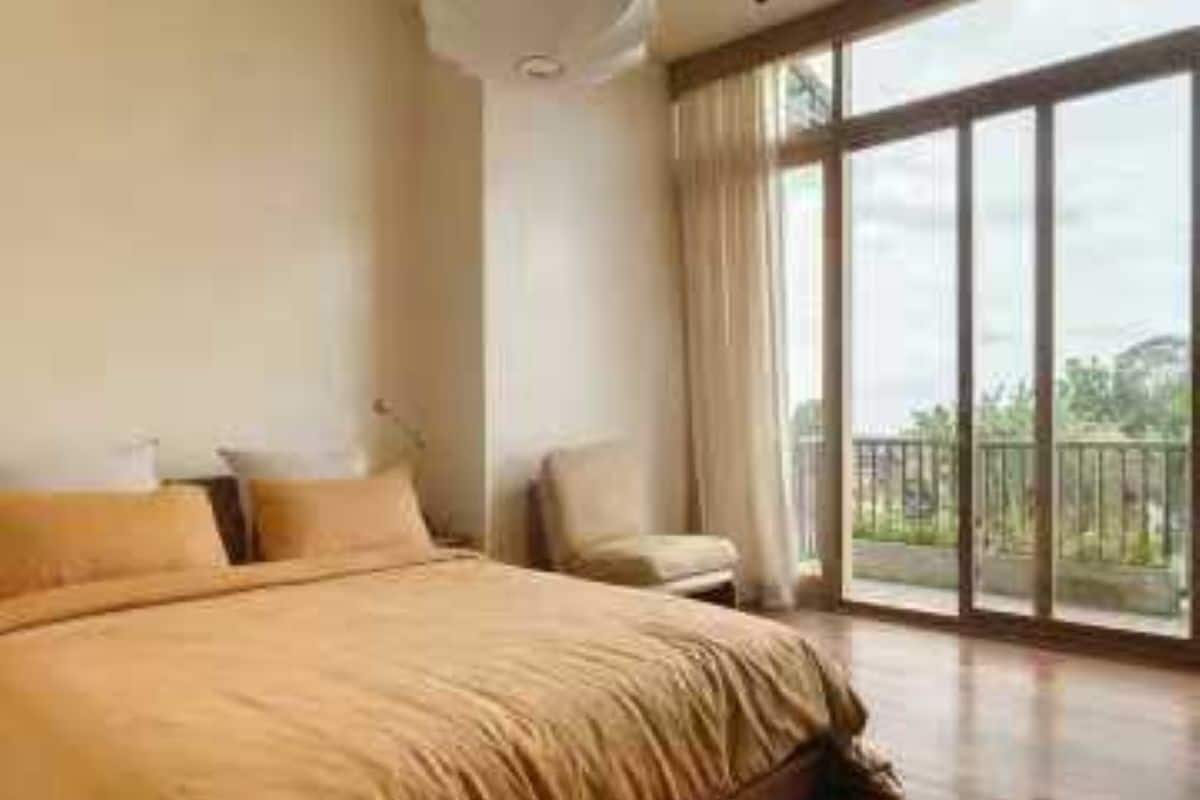 A bedroom with a large bed, a chair, and a balcony with a view.