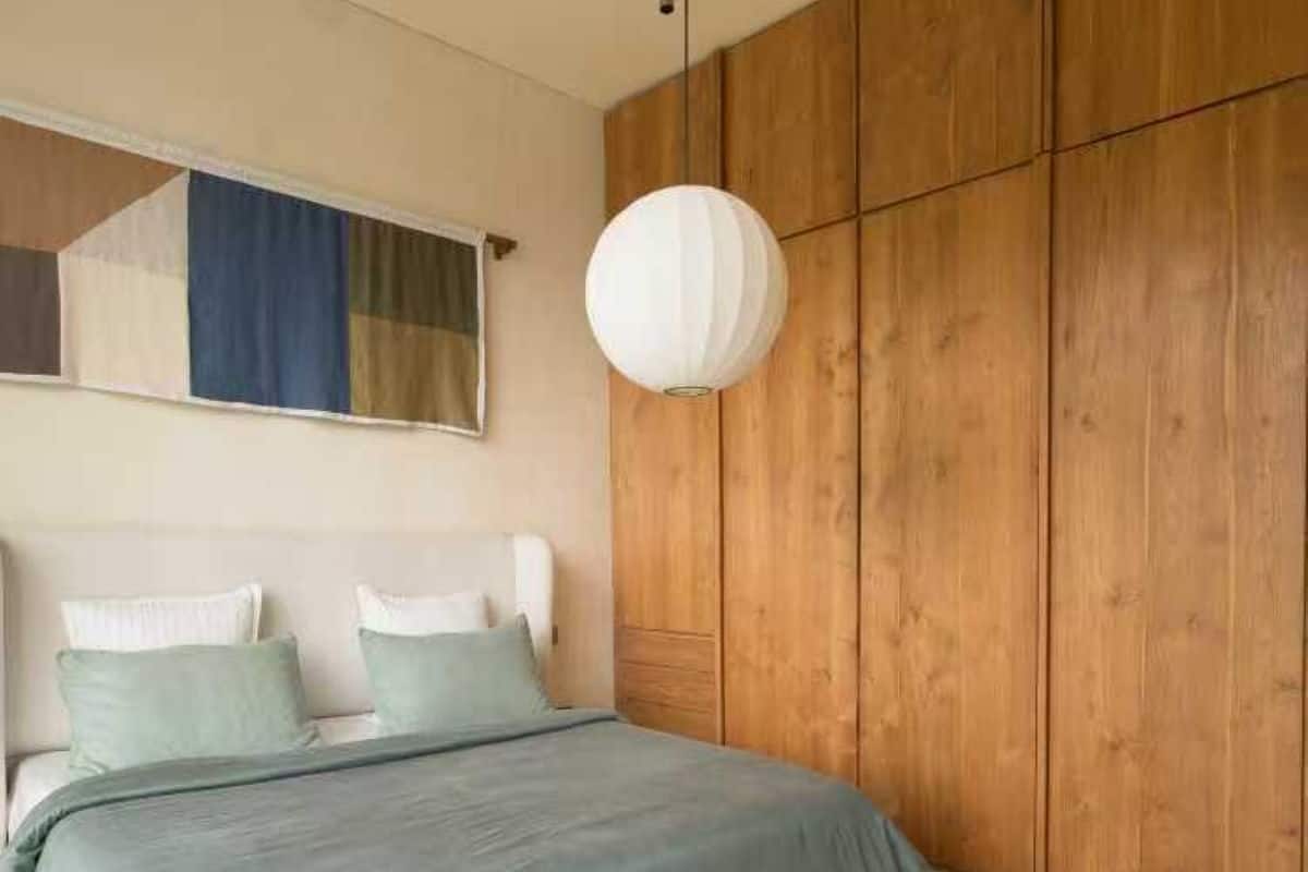A bedroom with a bed, wooden wardrobe, and a hanging light fixture.