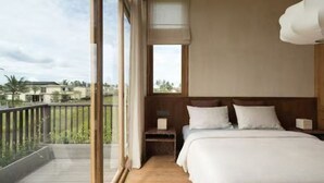 A bedroom with a large window, wooden flooring, a bed with white bedding, and a nightstand with a lamp. - KOO villa (Pejeng Kawan)