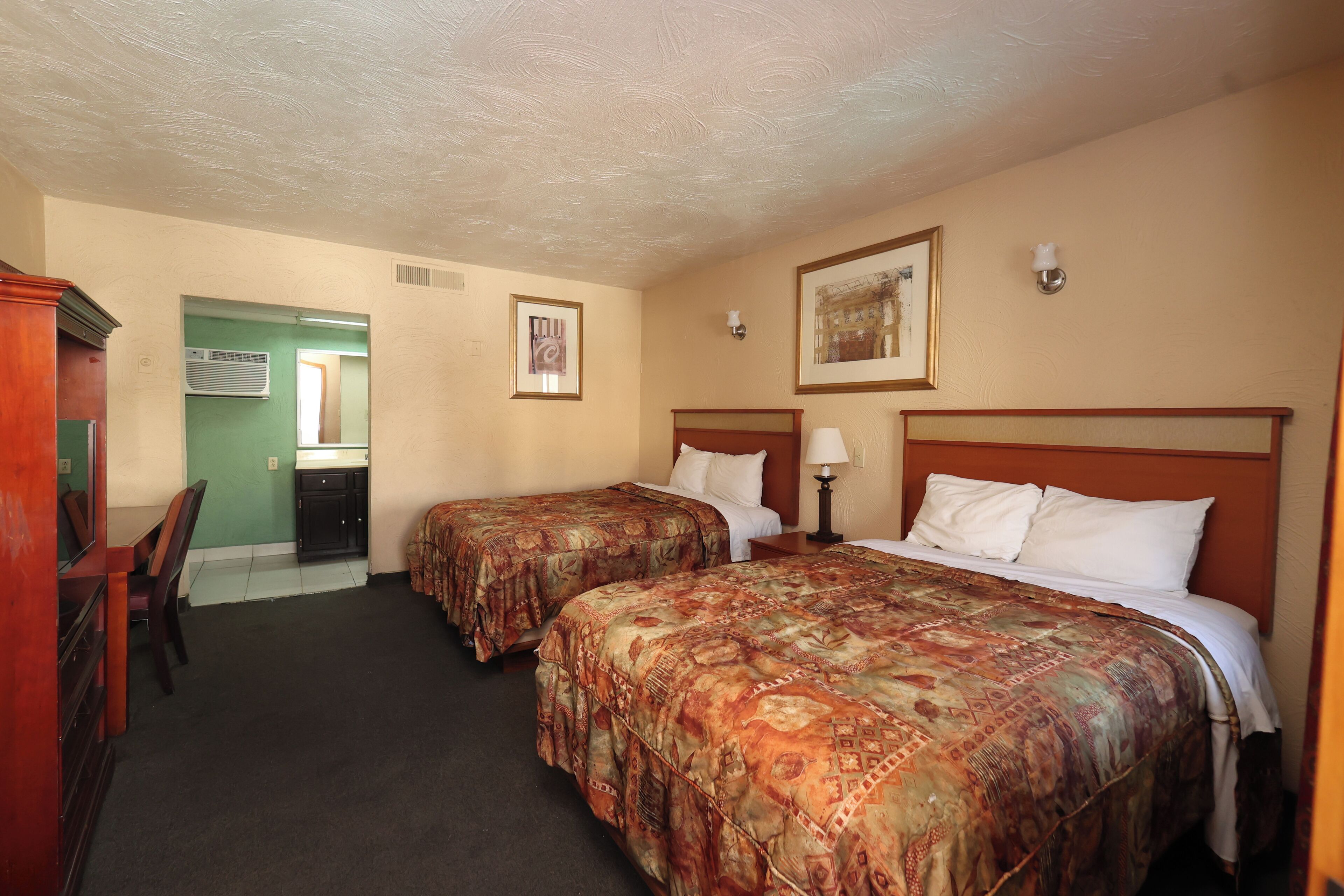 A hotel room with two beds, a desk, a chair, and a bathroom door.