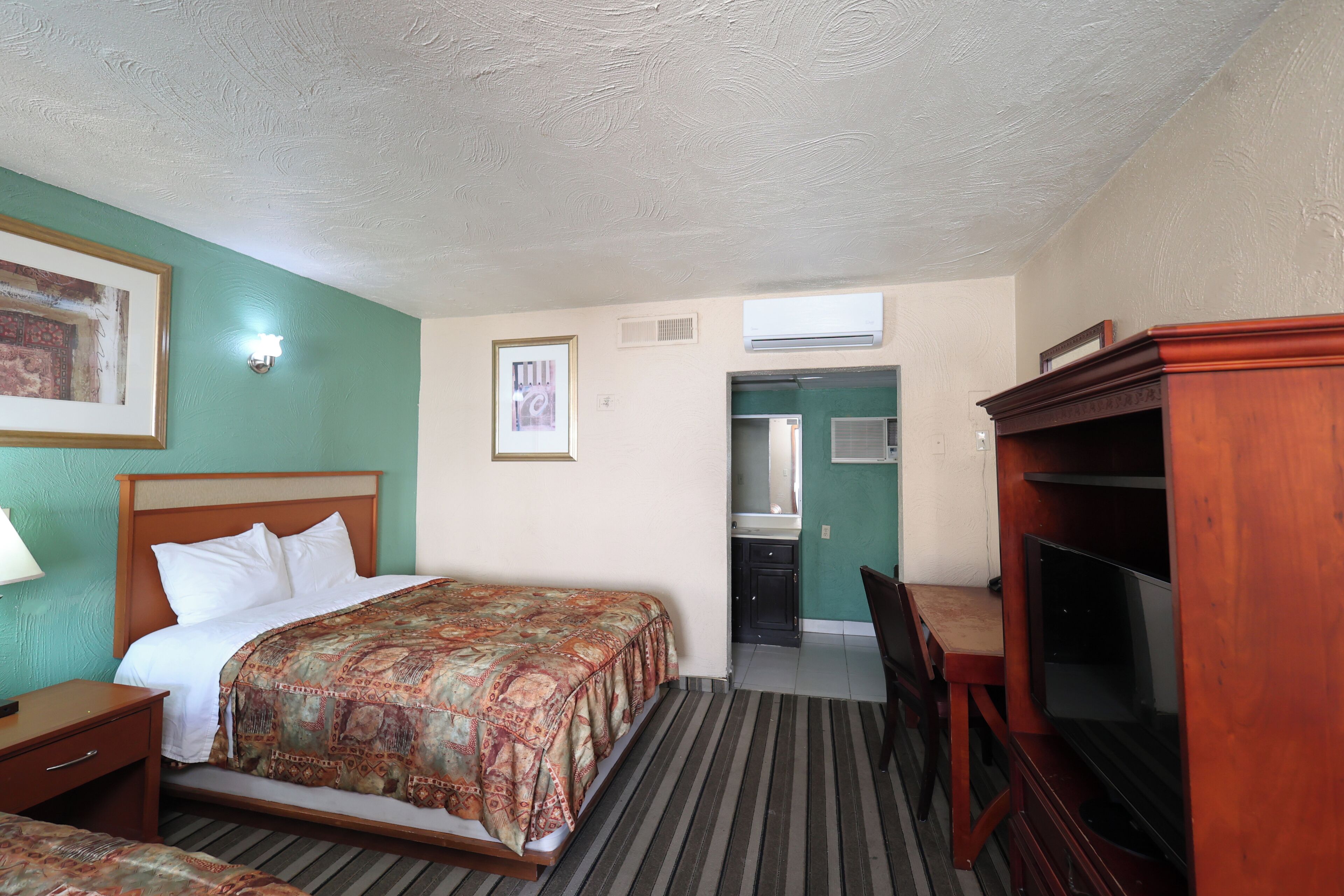Ein Hotelzimmer mit Bett, Schreibtisch, Stuhl, Fernseher und einem durch eine offene Tür einsehbaren Badezimmer.