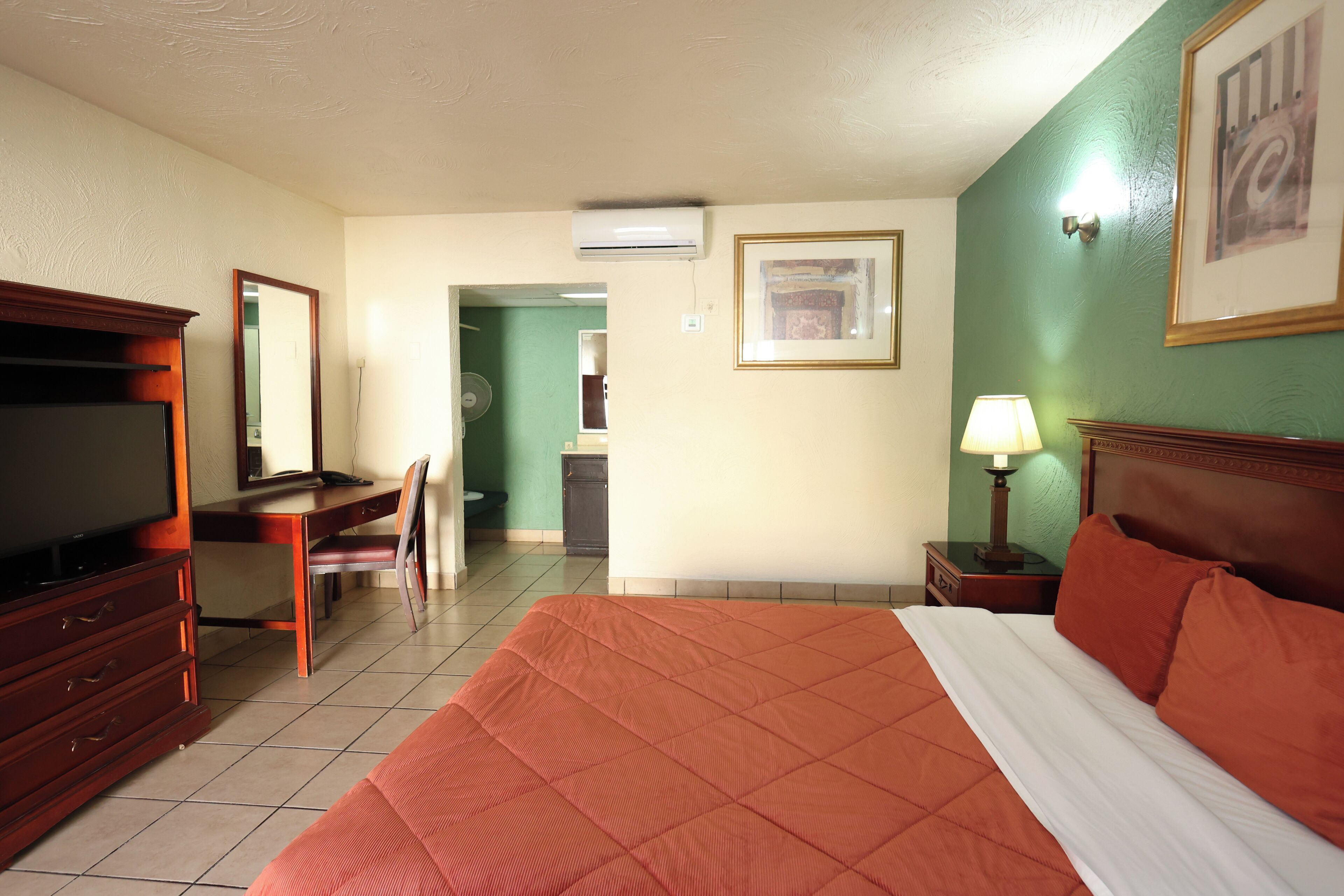 A hotel room with a bed, a desk, a chair, a television, a lamp, and a framed picture on the wall.