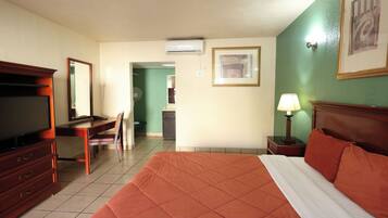 A hotel room with a bed, a desk, a chair, a television, a lamp, and a framed picture on the wall.