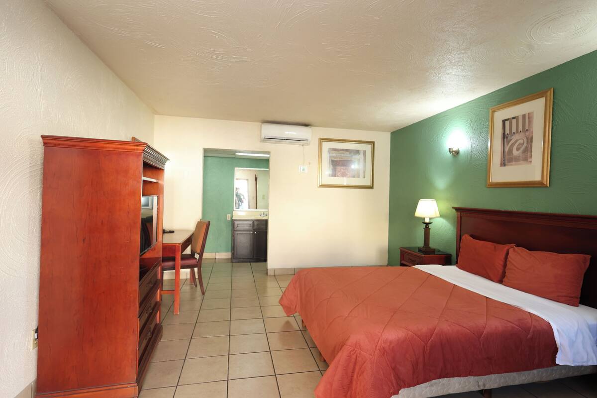 Ein Hotelzimmer mit Bett, Schreibtisch, Stuhl, Kommode, Nachttisch und Lampe.