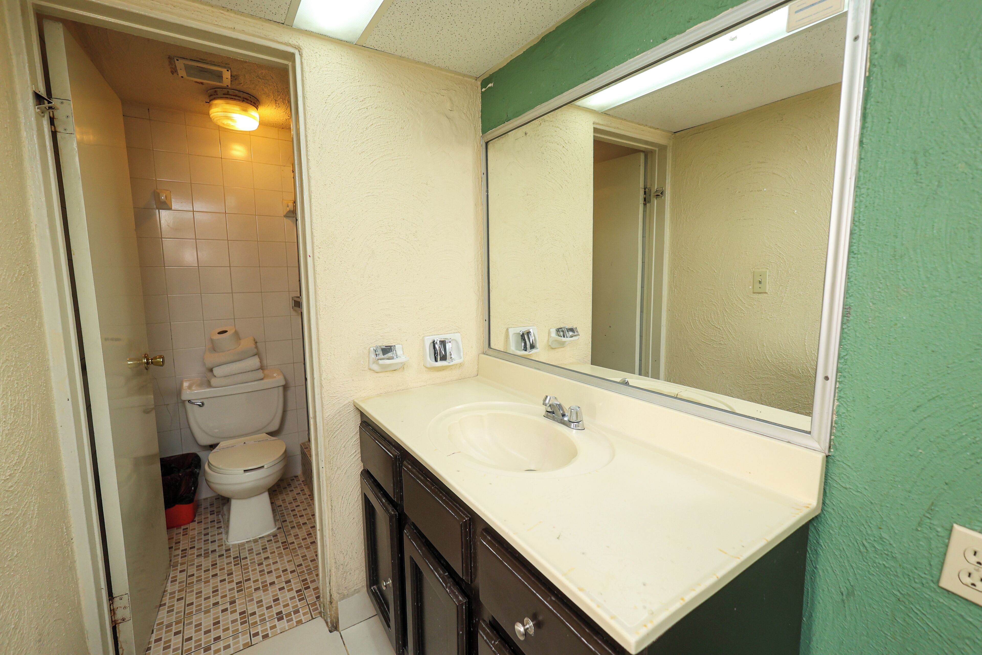 Un baño con lavamanos blanco, muebles oscuros, un espejo y un inodoro.