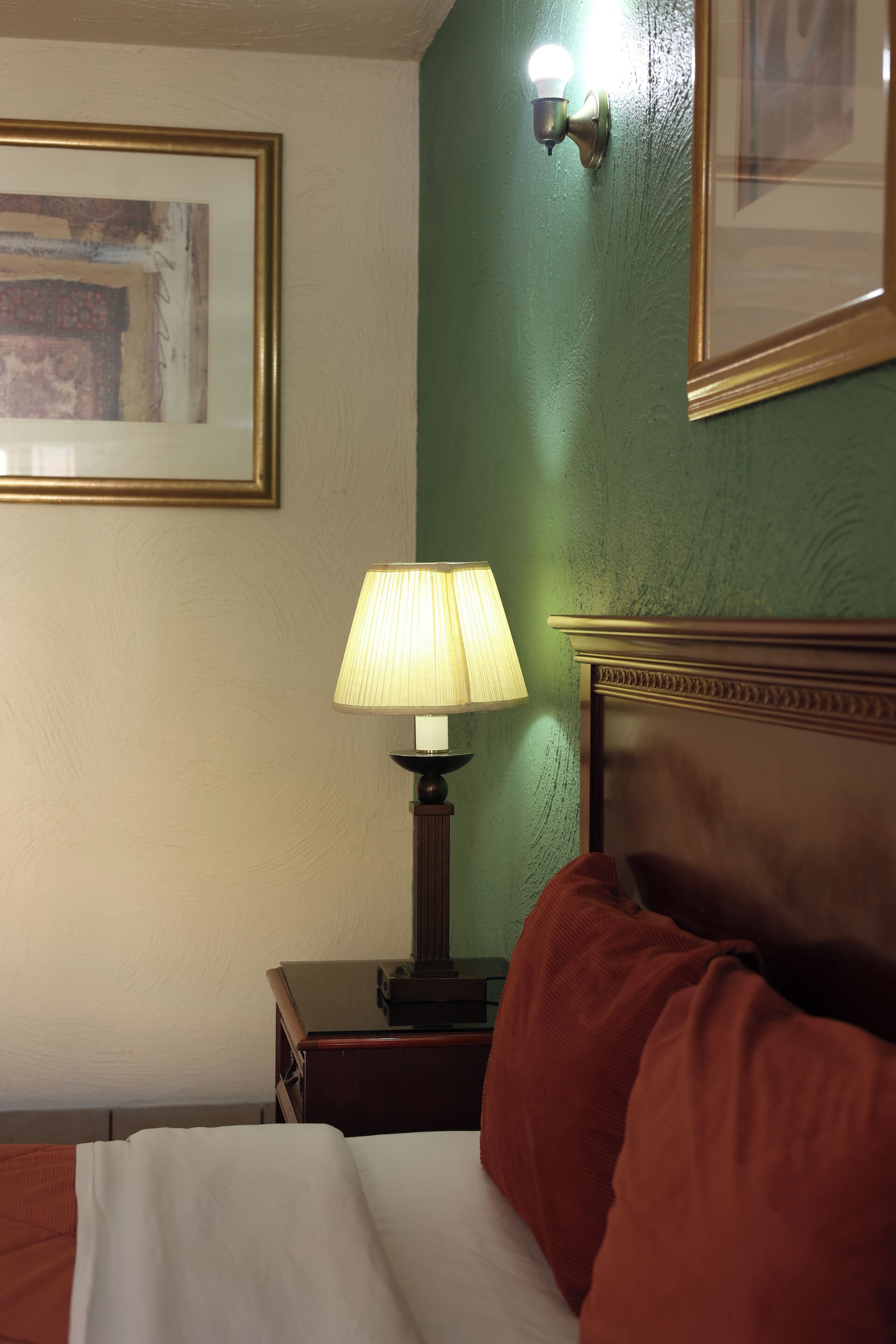 Ein Hotelzimmer mit einem Bett, einem Nachttisch mit Lampe, einem gerahmten Bild an der Wand und einer grünen Akzentwand.
