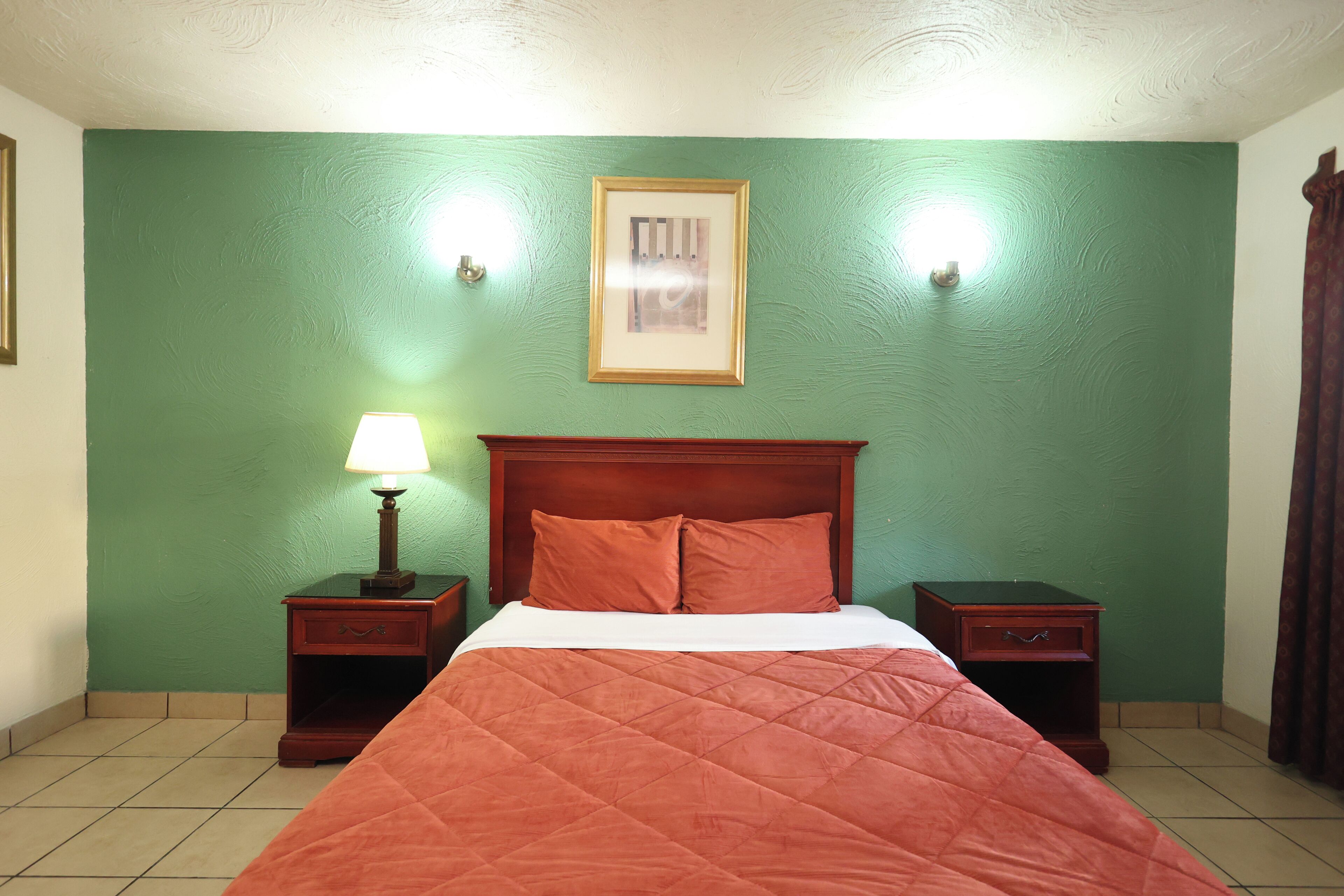 A room with a bed, green walls, a framed picture, and two nightstands with lamps.