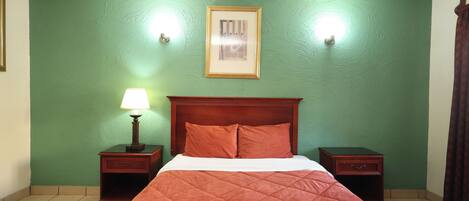 Una habitación con cama, paredes verdes, un cuadro enmarcado y dos mesitas de noche con lámparas.