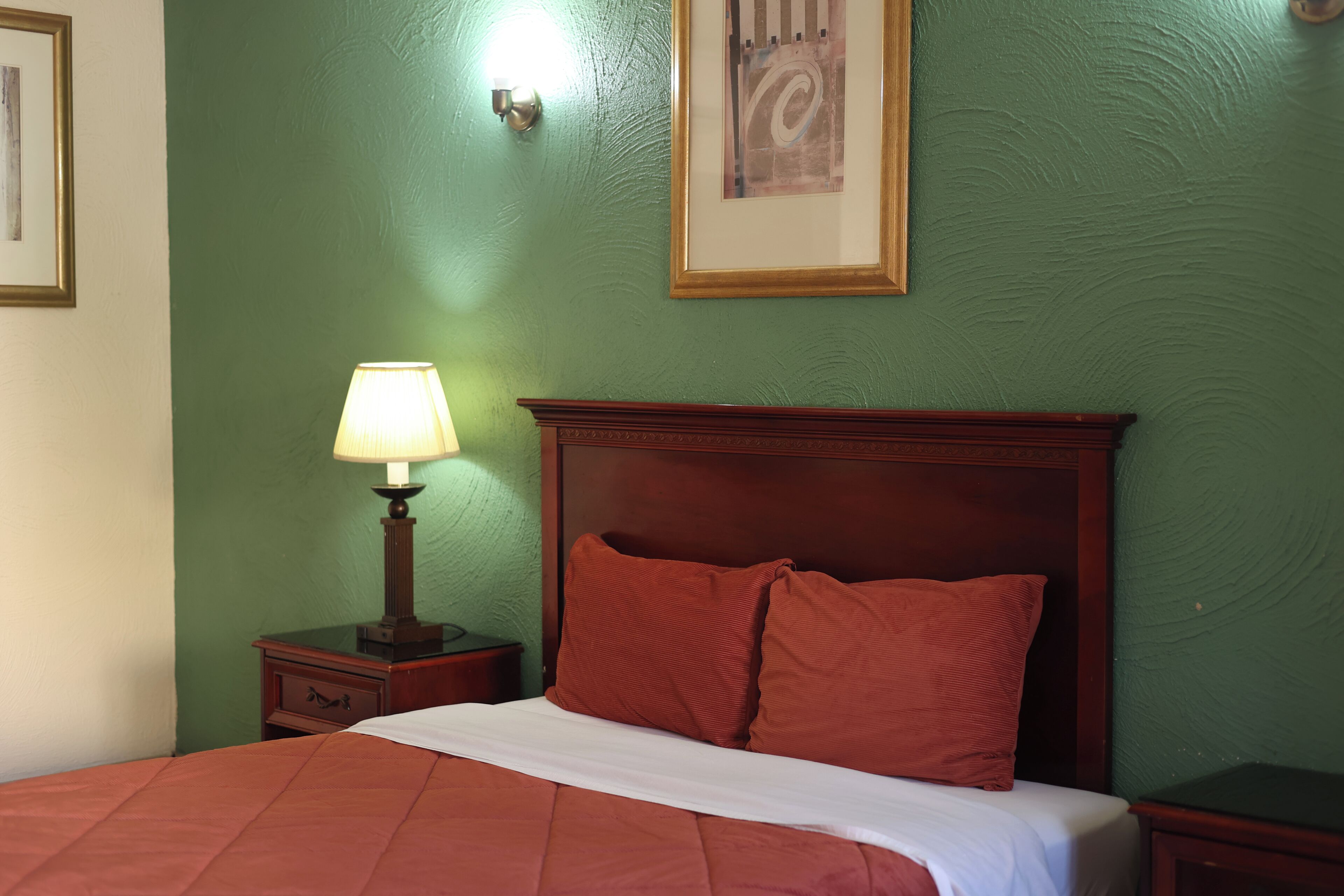 A neatly made bed with a wooden headboard, a bedside table with a lamp, and a framed picture on the wall.